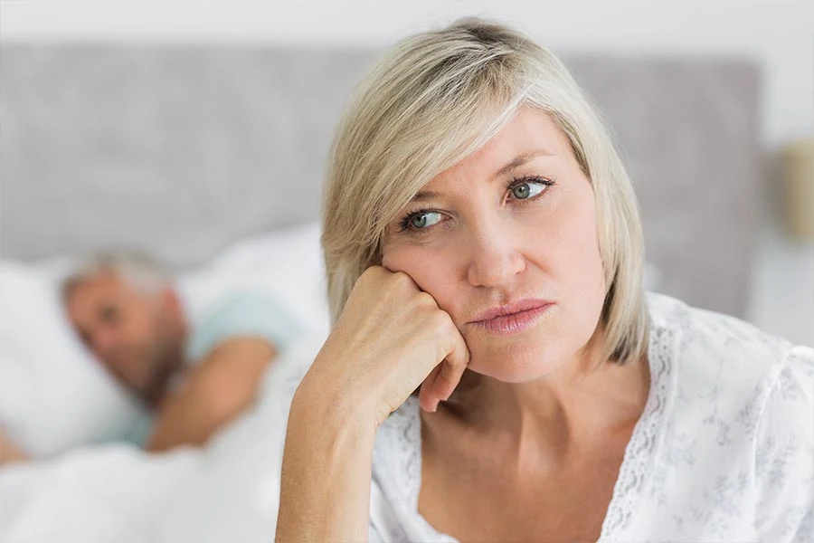 Mulher acordada na cama, de costas para o marido que dorme